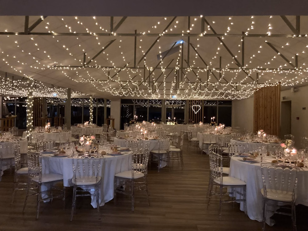 Ciel étoilé de guirlandes LED tendu sous le plafond d'une salle de réception de mariage, tables rondes dressées